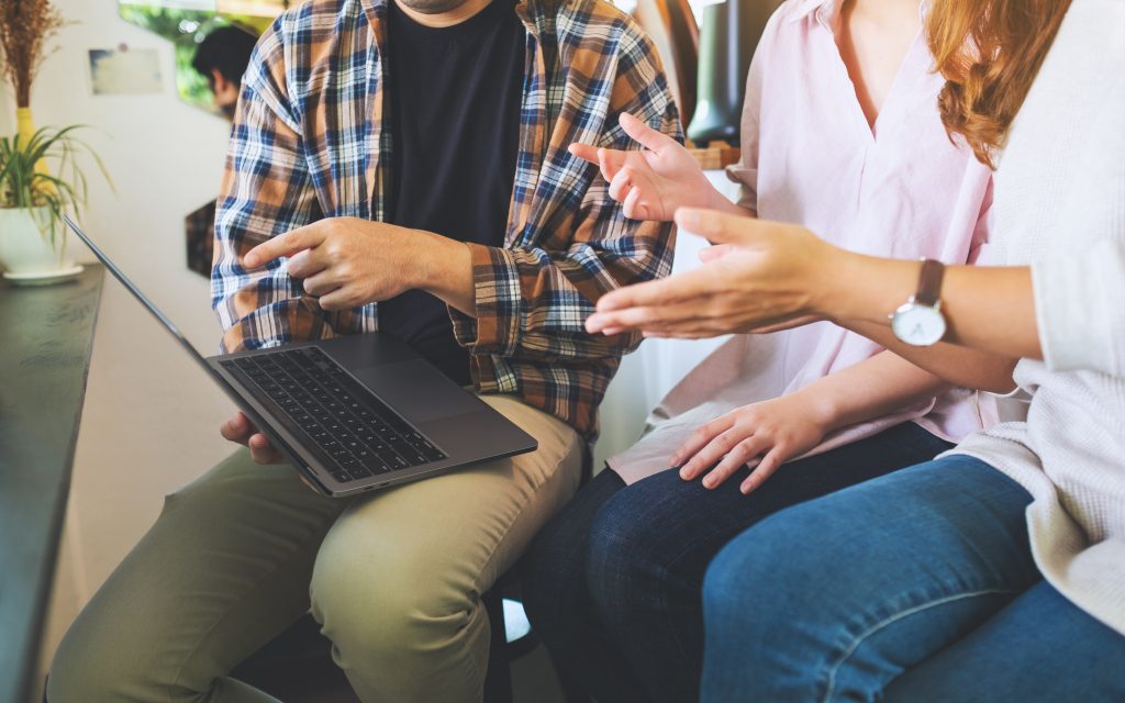 Tre unge folk snakker omkring en opgave, og peger på en Macbook pro